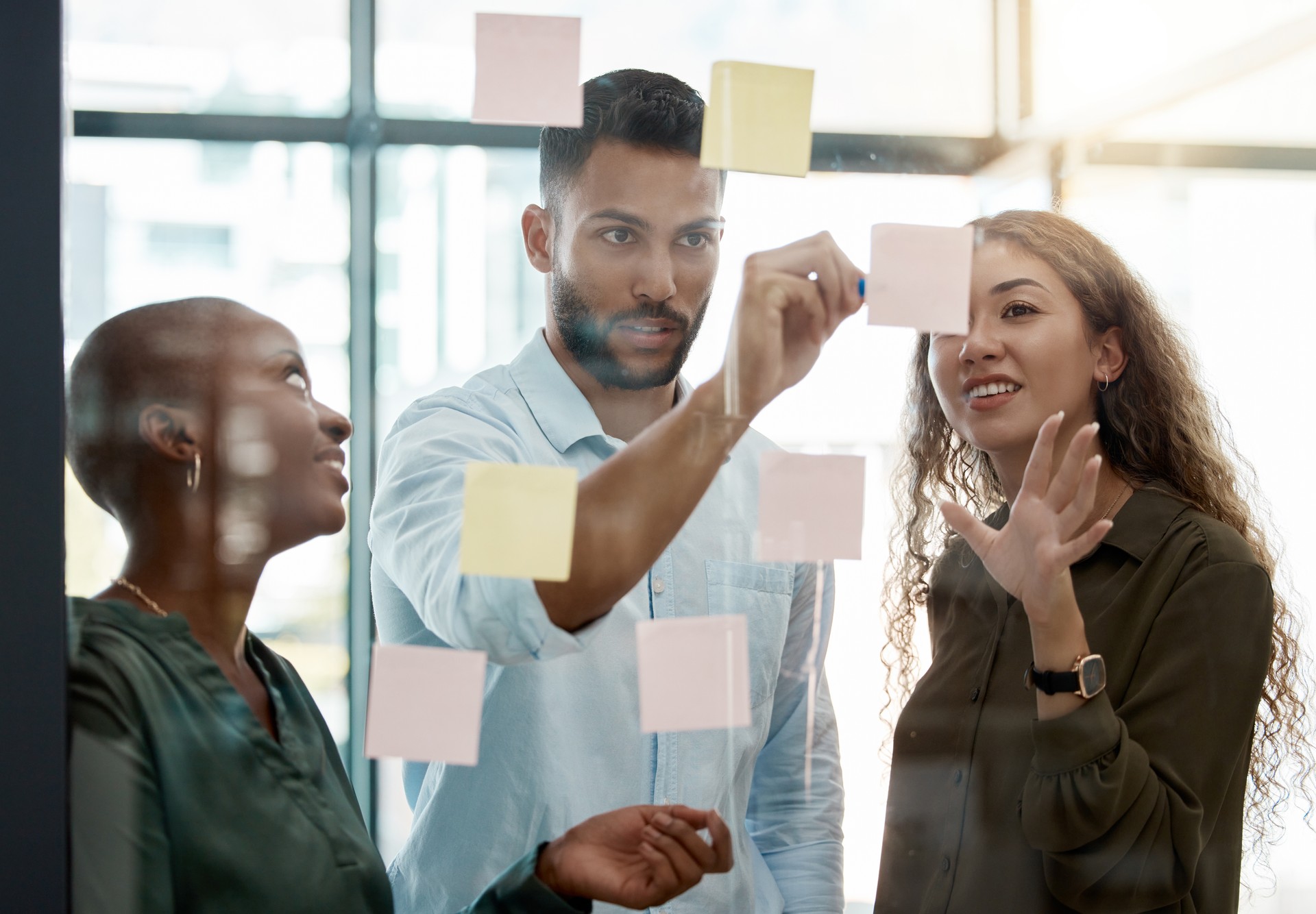 Team strategy meeting on research, post it on glass wall and group work planning together. Business people brainstorming analytics vision think tank ideas, collaboration thinking and sticky notes